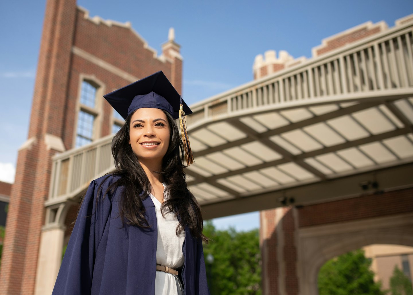 Graduate in navy cap and gown standing on university campus.