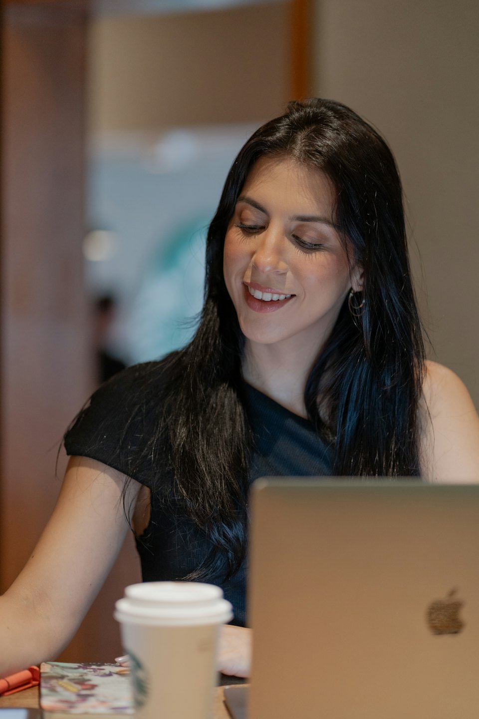 Woman smiling while working on a laptop at a cafe.
