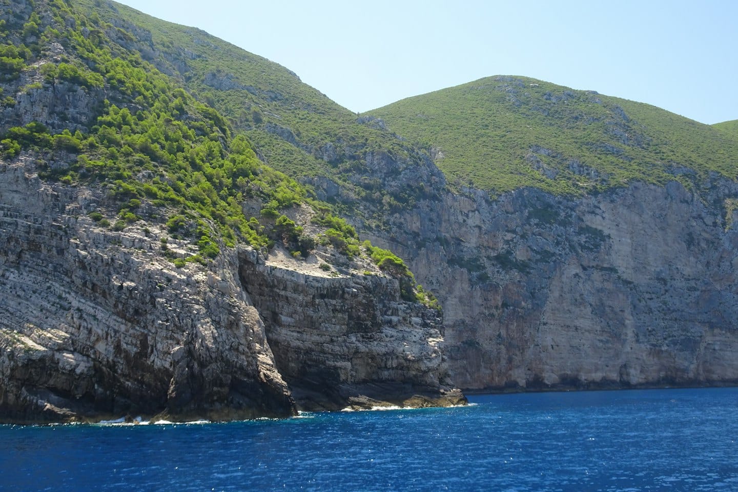 Steep rocky cliffs with green vegetation rise from the sea.