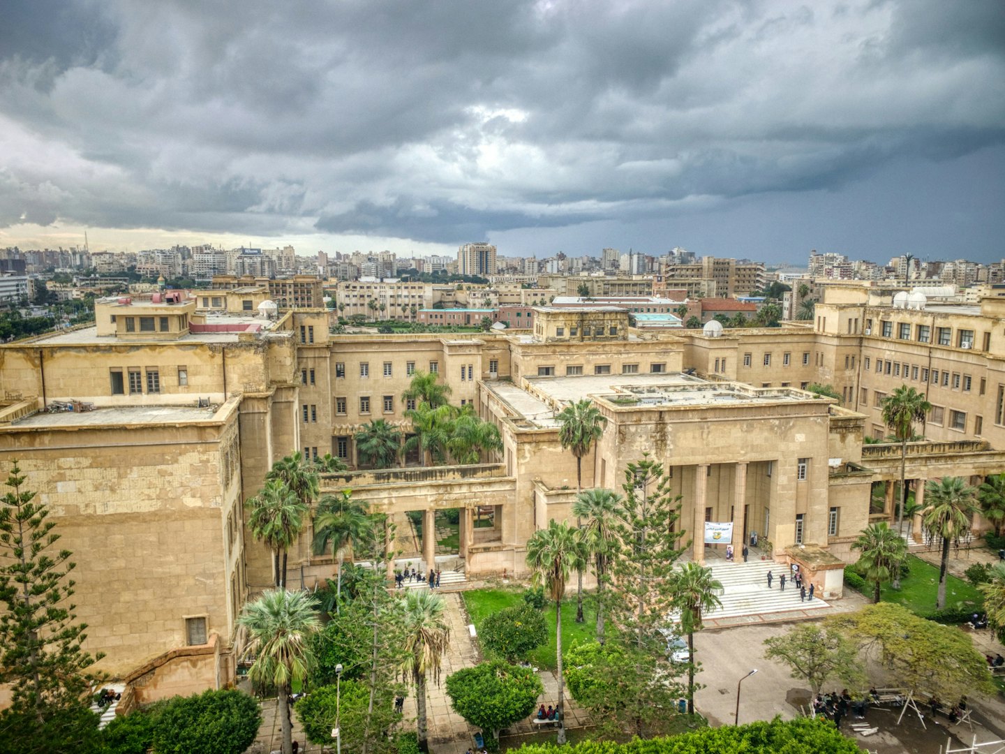 Sandy-colored university campus with palm trees and people on paths.